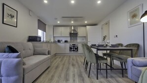 A modern living room with a sofa, a dining area with chairs, and a kitchen in the background.