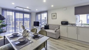 A modern kitchen with a dining area, a sofa, and a TV.