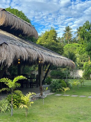 A thatched-roof structure with outdoor seating, surrounded by lush greenery and palm trees. - A Calm and Comfortable Beachfront Getaway (Zamboanguita)