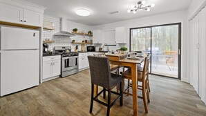 Eine moderne Küche mit weißen Schränken, ein Essbereich mit Holzmöbeln und eine große Schiebeglasdoor, die auf eine Terrass führt.