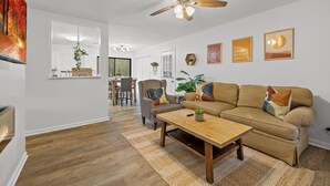 Ein Wohnzimmer mit Couch in Beige, Holztisch und Deckenventilator.