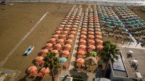 An aerial view of a beach with rows of umbrellas and beach chairs, a lifeguard tower, and a boat on the sand. - Homiday - Residence Venere, Interior 7 (Alba Adriatica)