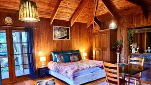 Ein Schlafzimmer in einer Holzhütte mit einem Bett, einem Esstisch und Blick ins Freie.