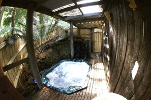 A hot tub area with a stone wall, wooden deck, and a covered roof structure. - Forget Me Not Cottages-Music Room (Warburton)