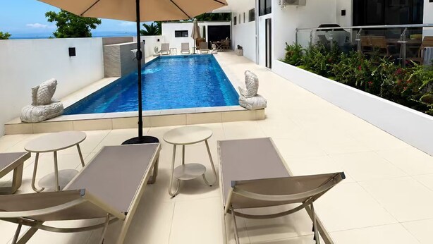 Un área de piscina moderna al aire libre con sillones de descanso, una sombrilla grande y una vista despejada del cielo.