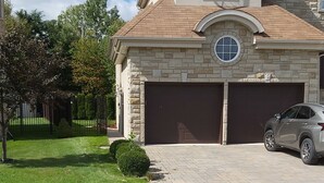 A residential house with a stone facade, two garage doors, a well-maintained lawn, and a parked car.
