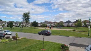 A residential street with houses, a playground, and a car parked on the side.