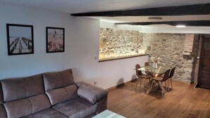 Una sala de estar con sofá, una mesa de comedor con sillas, una pared de piedra y una viga de techo de madera.