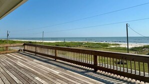 Eine Holzterrasse mit Geländer, die auf einen Strand blickt.