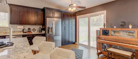 A modern kitchen with dark wooden cabinets, a stainless steel refrigerator, a marble countertop, and a built-in piano.