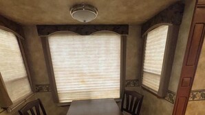 A compact RV interior with a dining table and two chairs, a ceiling light fixture, and two windows with blinds. - Spacious RV with AC in charming Holly Beach (Lake Charles)