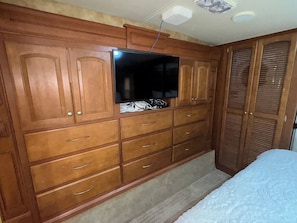 A bedroom with a wooden wardrobe, a bed, and a television mounted on the wall.