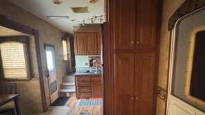 A narrow RV kitchen with wooden cabinets, a white refrigerator, and a window providing natural light. - Spacious RV with AC in charming Holly Beach (Lake Charles)