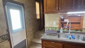 A compact kitchen with wooden cabinets, a sink, and a small countertop. - Spacious RV with AC in charming Holly Beach (Lake Charles)