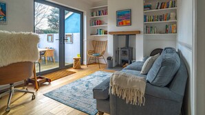 Een gezellige woonkamer met een bank, een fauteuil, een boekenkast en een open haard.