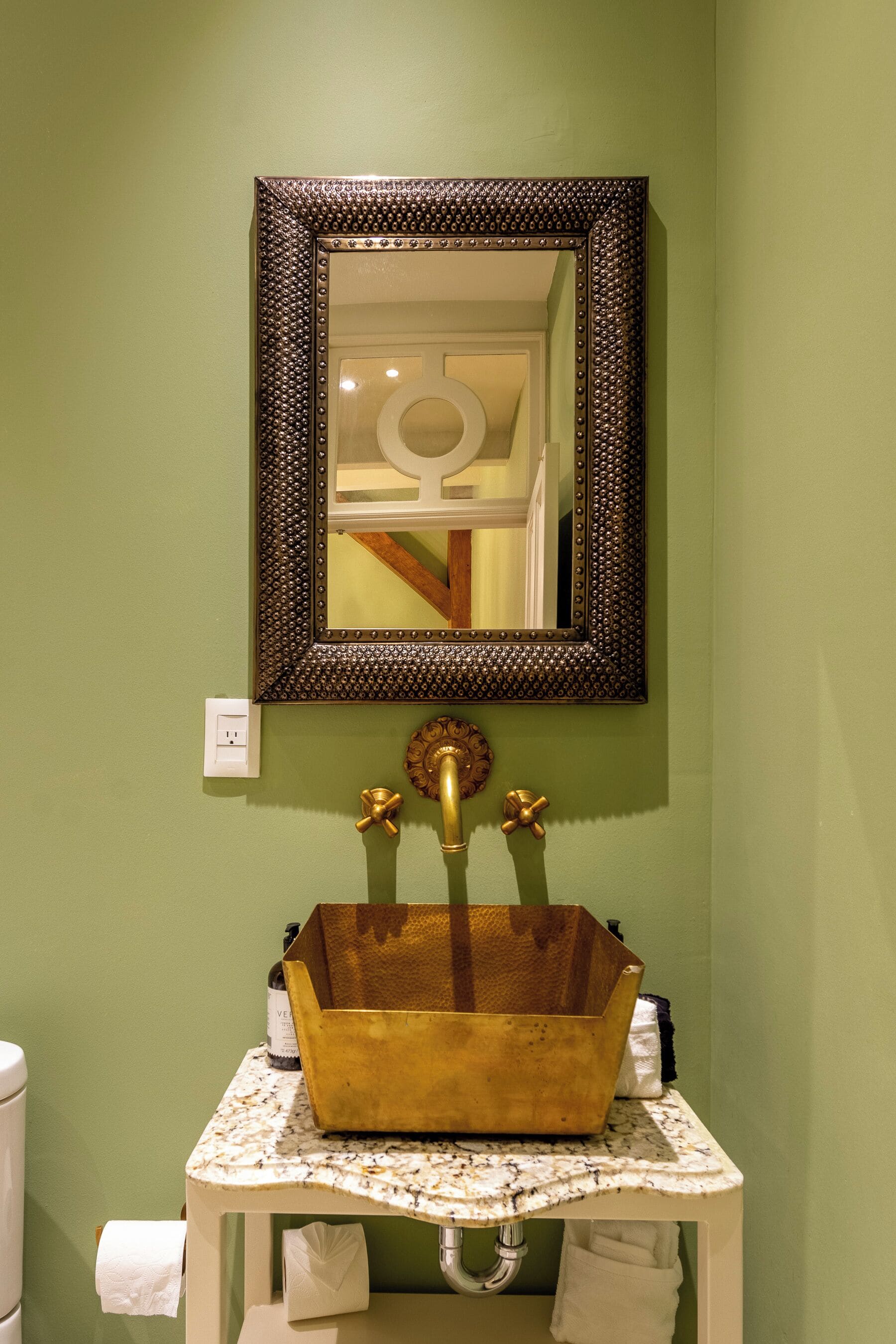 A bathroom with a green wall, a white sink with a gold basin, and a mirror with a decorative frame.