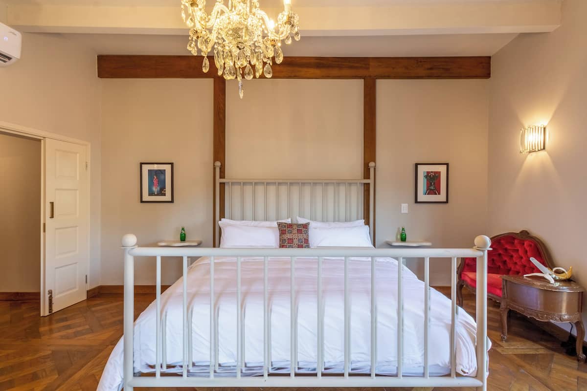 Un dormitorio con una cama blanca, vigas de madera, una araña y un sillón rojo.