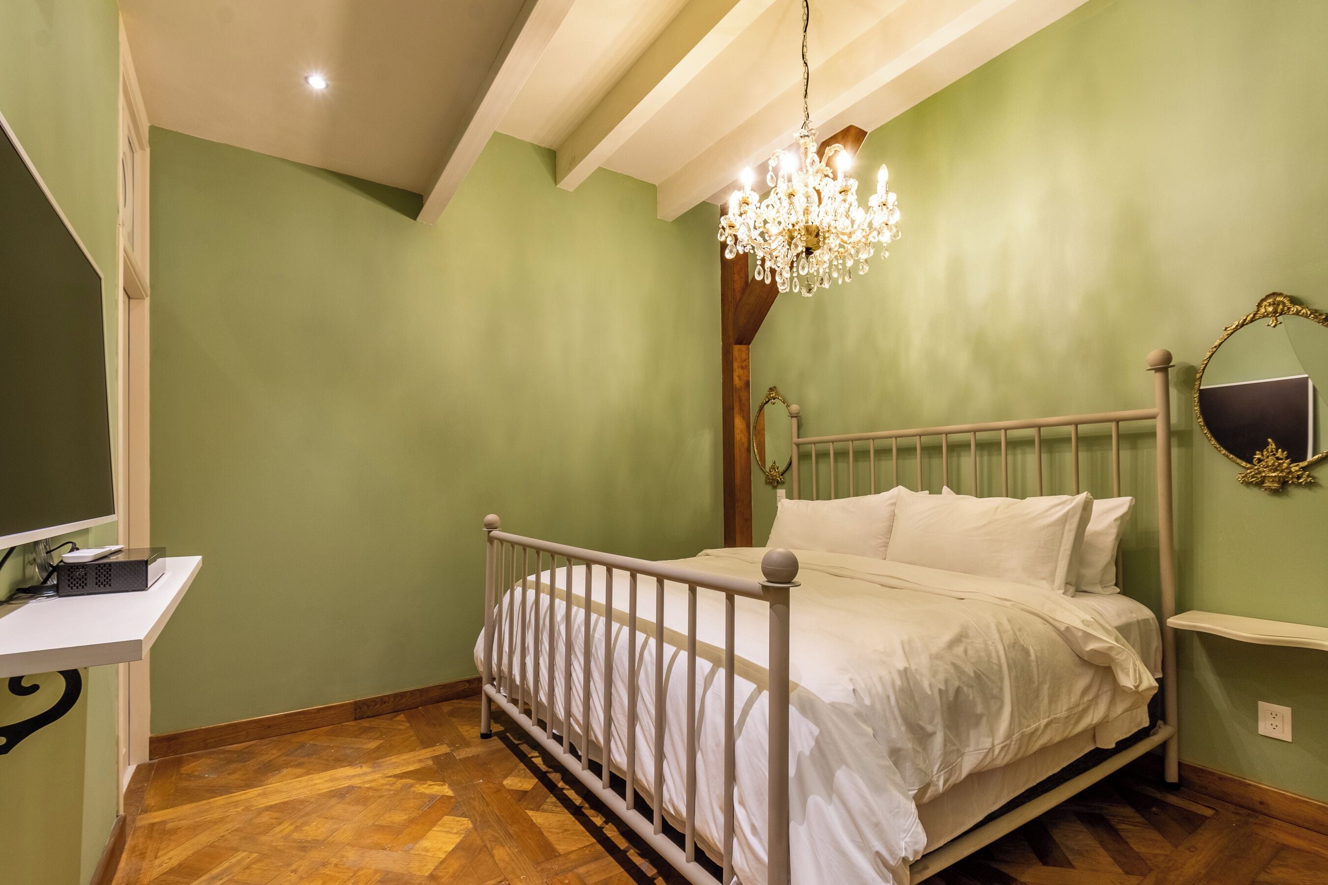 Een slaapkamer met een bed, nachtkastje, spiegel en een kroonluchter.