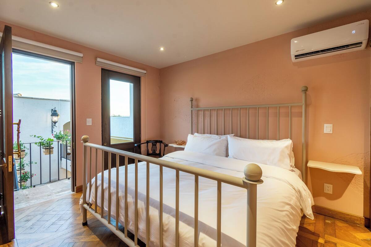 Un dormitorio con cama, mesita de noche, ventana y aire acondicionado.