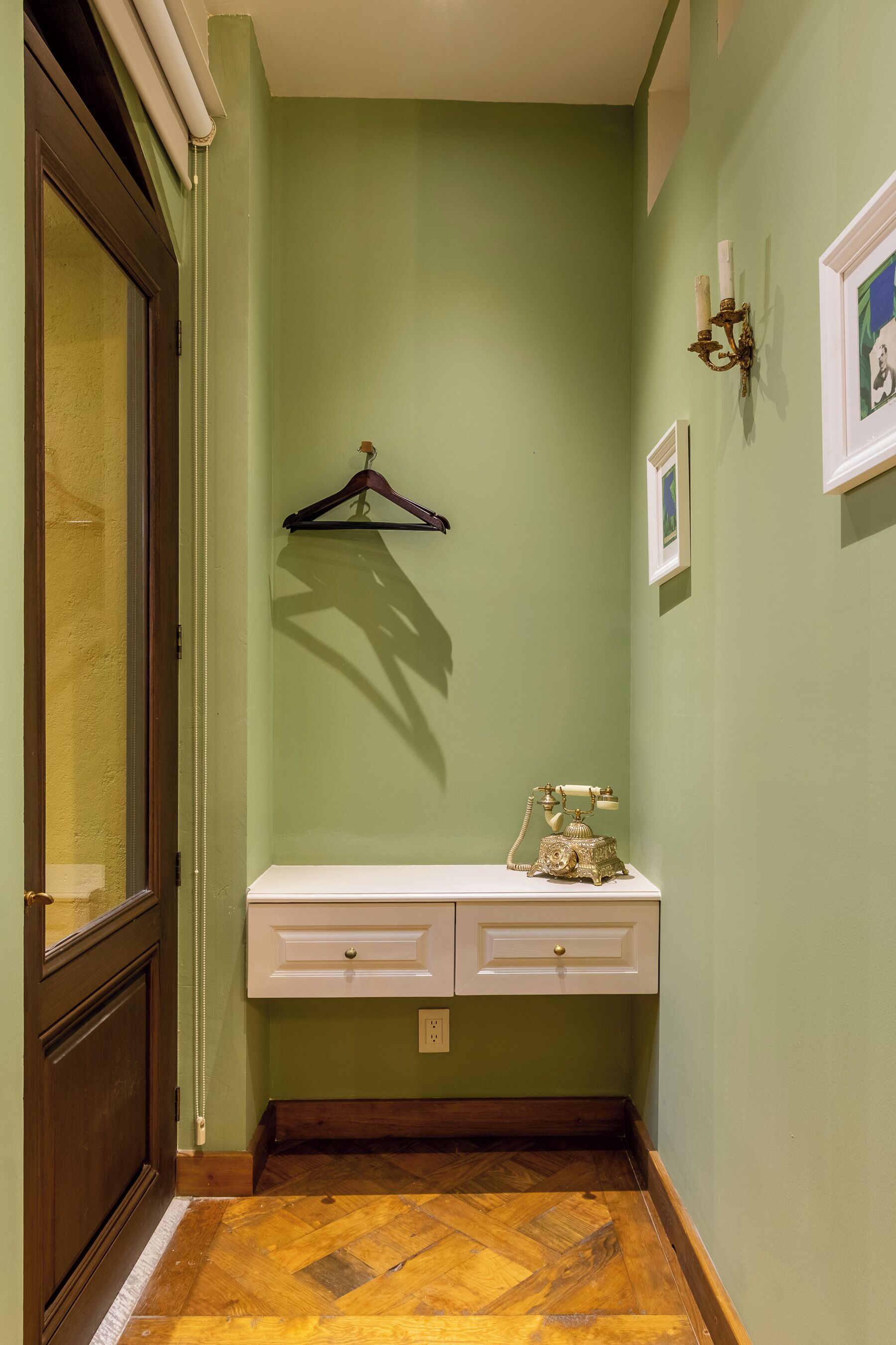 A hallway with a wooden floor, a white console table with drawers, a hanging coat rack, and a wall-mounted telephone.