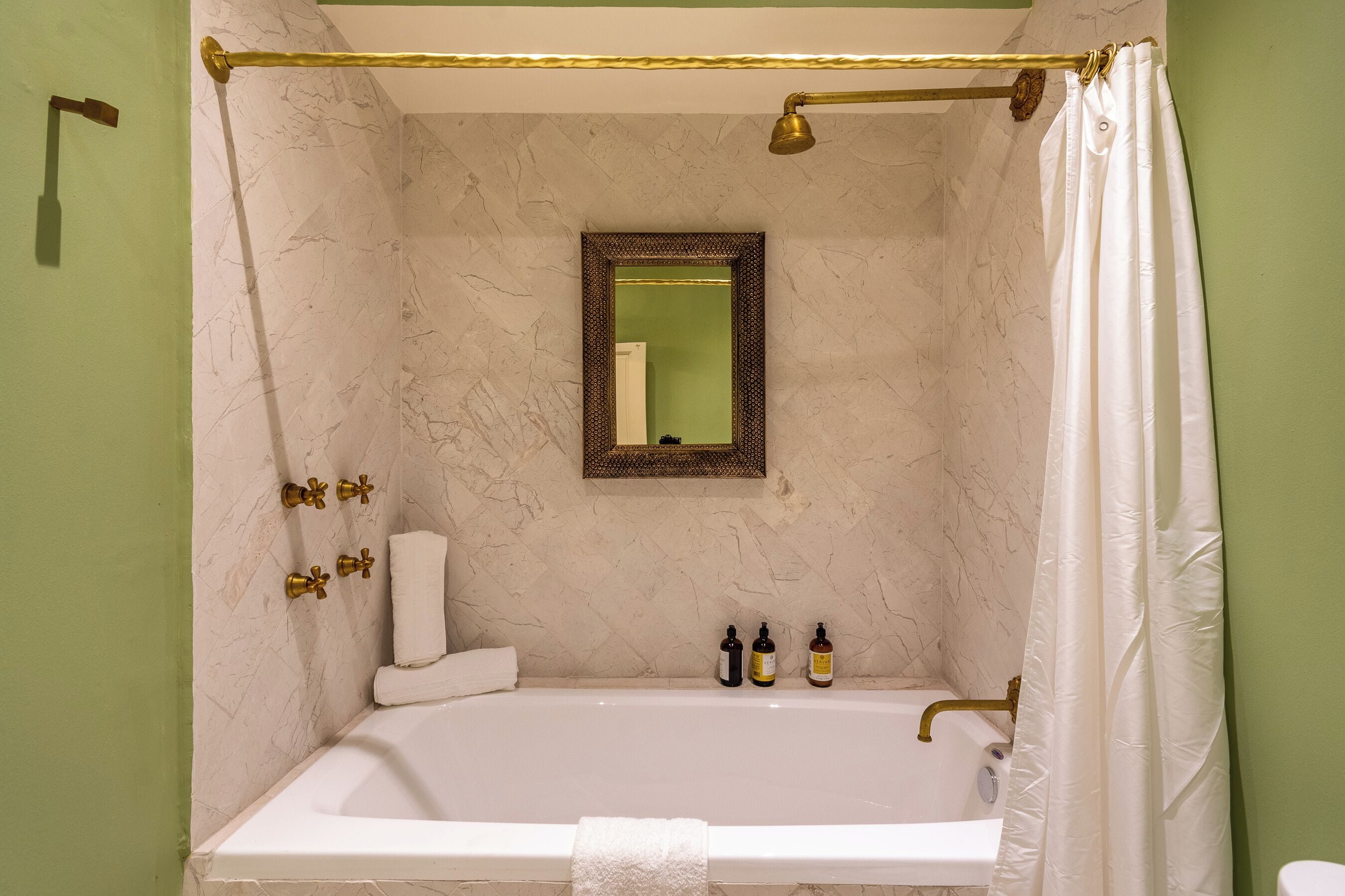 Un baño con bañera, cortina de ducha, espejo y dos botellas de champú.