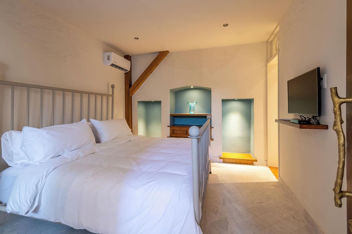 Un dormitorio con cama, televisor montado en la pared y una escalera que conduce a un nivel superior.