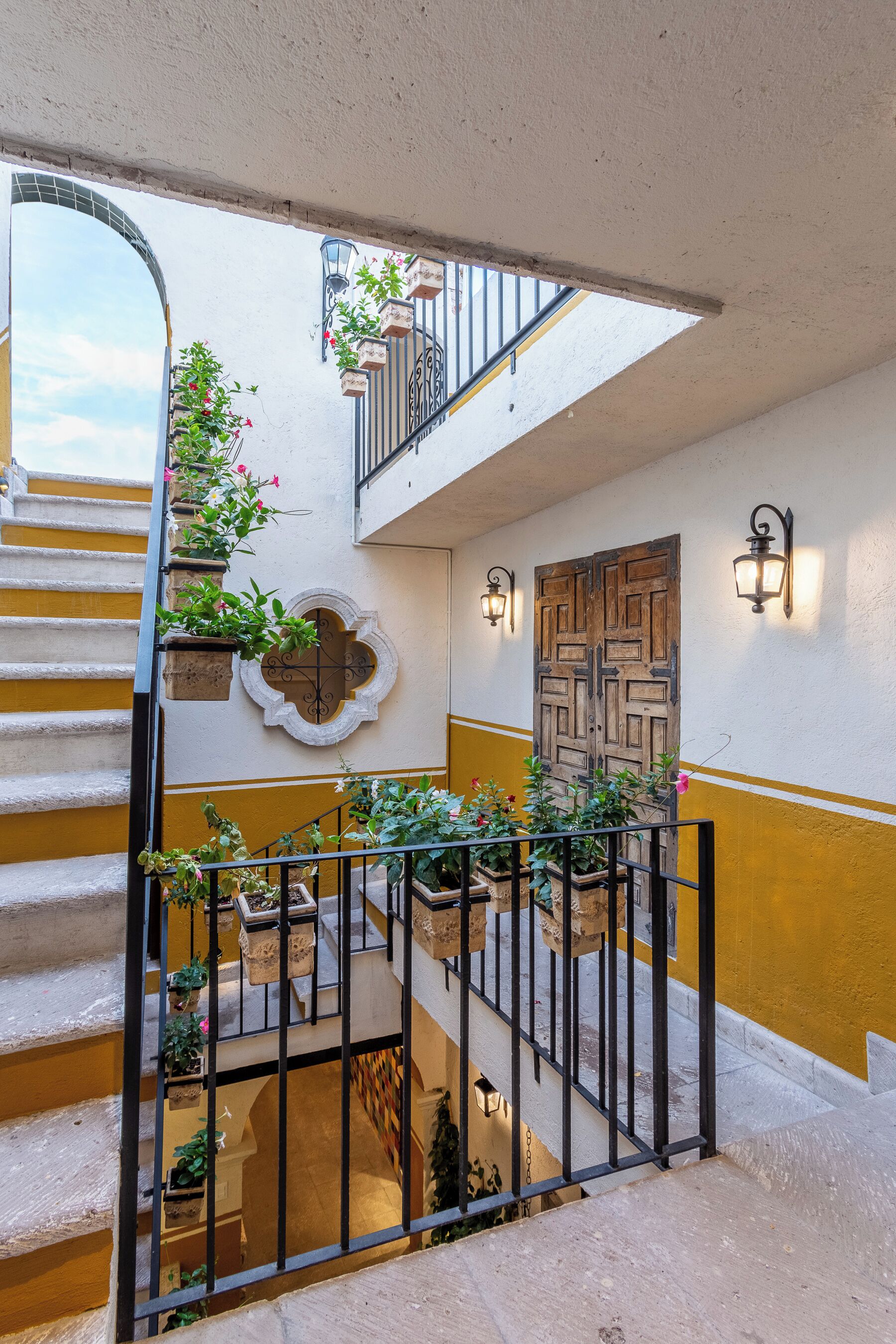 Un intérieur à plusieurs niveaux, avec un escalier, des plantes en pot et une porte décorative en bois.