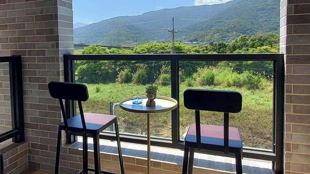 A balcony with two chairs and a small table, overlooking a mountainous landscape. - Bliss inn (Yuli)