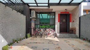 A covered outdoor area with a tiled floor, bicycles, and a door with a red frame. - Bliss inn (Yuli)