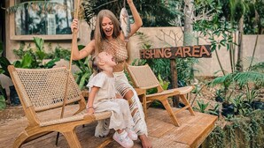 Une chaise-balançoire en bois avec un enfant et un adulte, un panneau indiquant « ZONE DE PÊCHE », et une végétation luxuriante en arrière-plan.