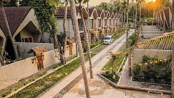 A resort with a fire pit area, palm trees, and a row of houses with a sunset in the background.
