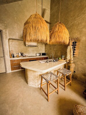 Una cocina moderna con una isla central, taburetes de madera y una lámpara colgante.
