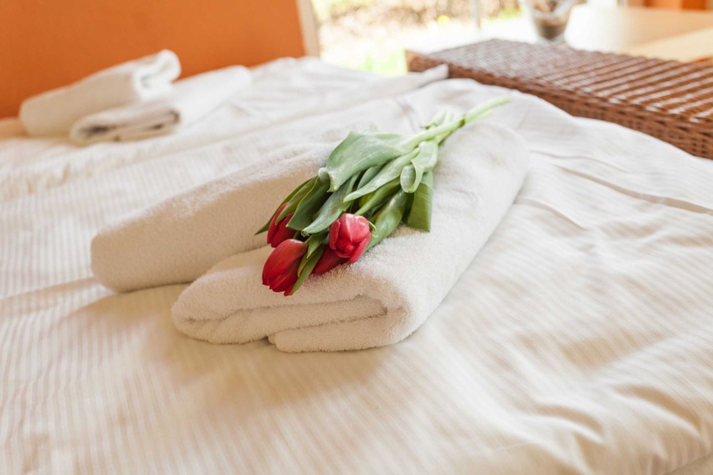 Un lit bien fait, avec des serviettes blanches et un bouquet de tulipes rouges.