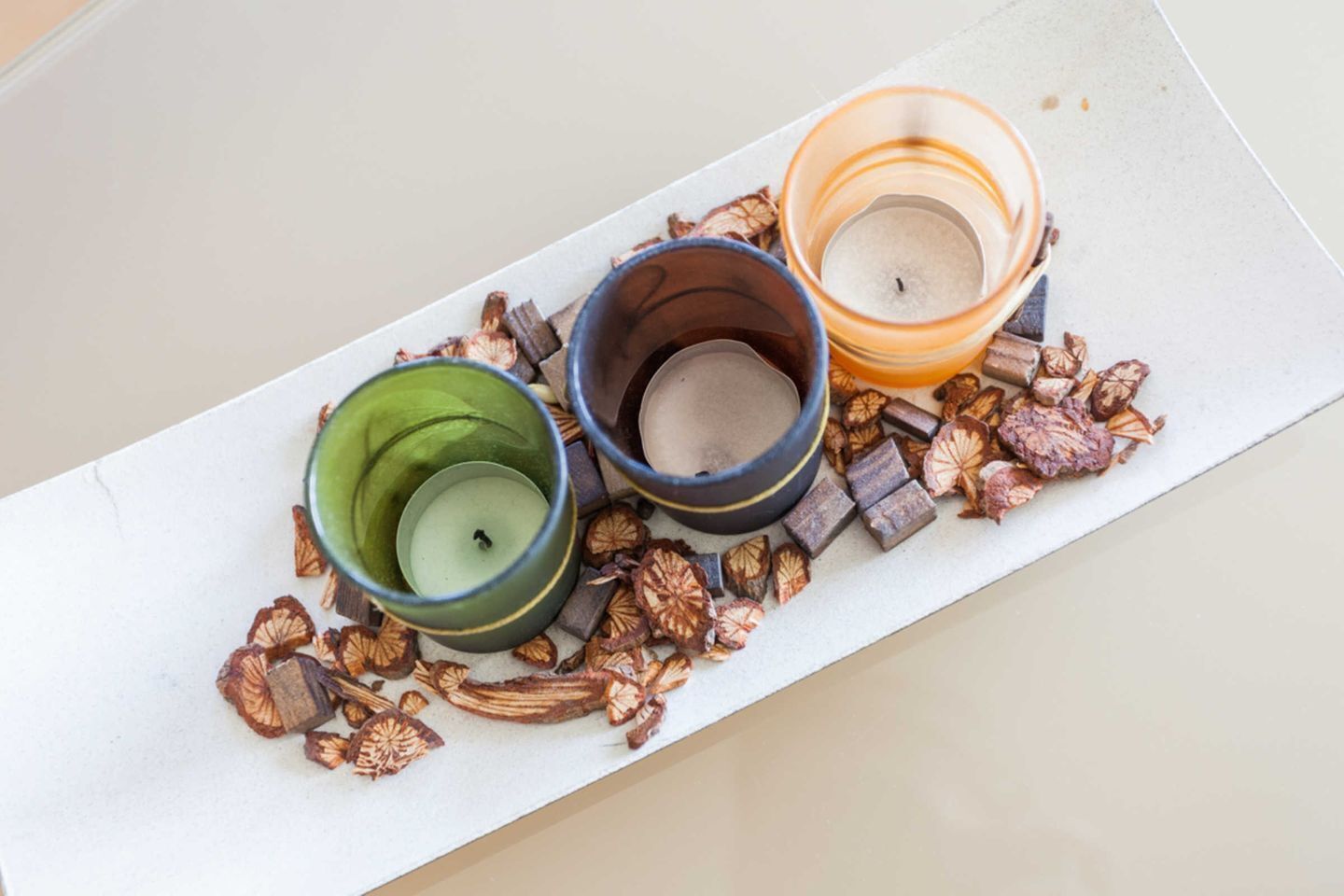 Three candle holders with dried flowers and spices on a flat surface.