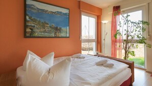 A hotel room with a large bed, a painting on the wall, and a window with a view of greenery.