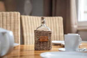 Eine Flasche Riviera Maison Wein in einem Korbflechtkorb auf einem Tisch mit weißen Tassen und Untertassen.