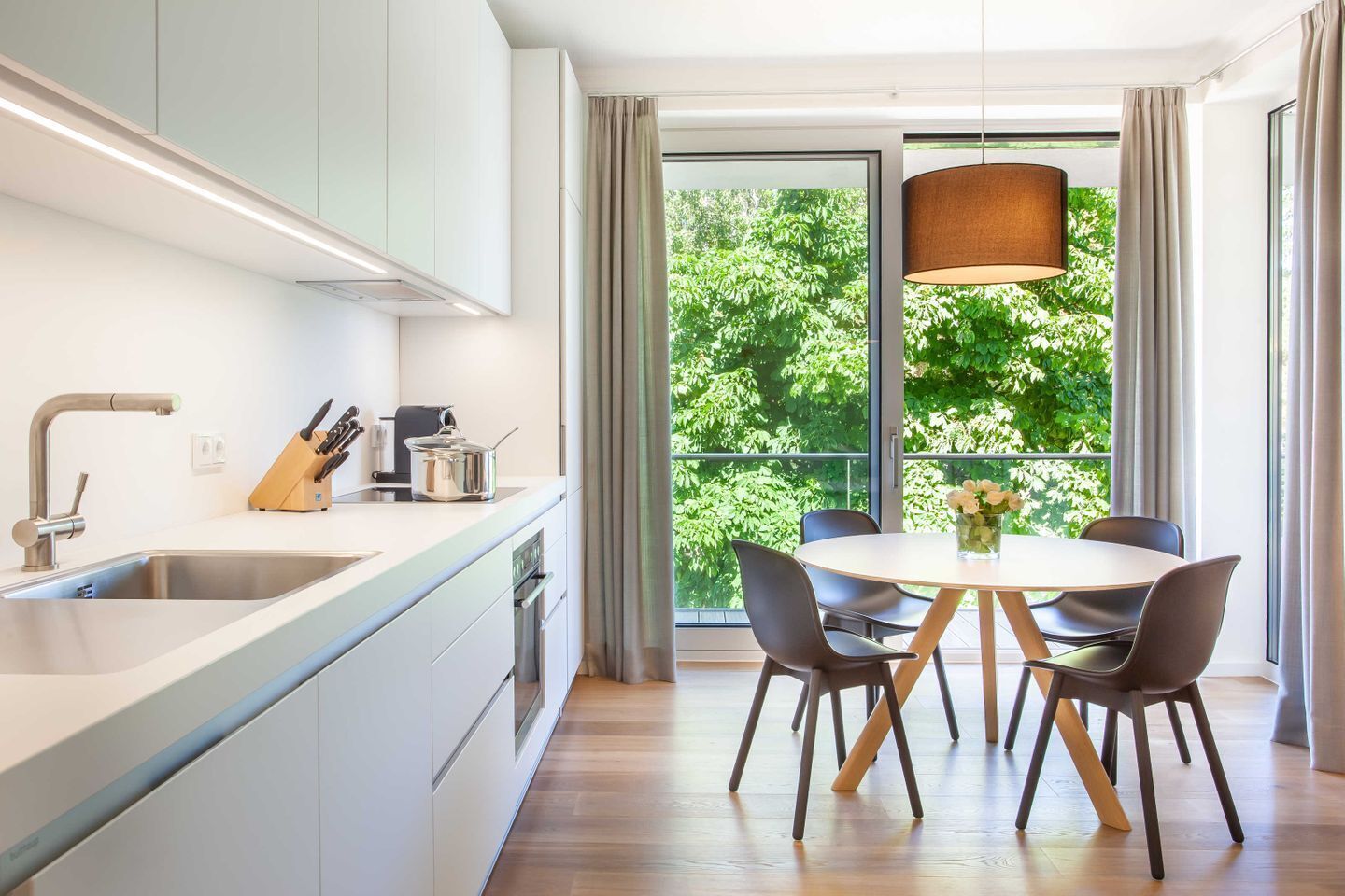 Et moderne køkken med et stort vindue, et spiseområde med et rundt bord og stole, samt en hængende lampe.