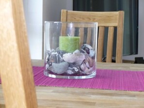 Un porte-bougie en verre contenant une bougie verte et des pierres, posé sur une table en bois avec un set de table violet.