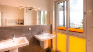 Ein modernes Badezimmer mit zwei Waschbecken, einem großen Spiegel und einem Fenster mit Jalousien.