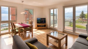 Ein geräumiges Wohnzimmer mit großem Fenster, Essbereich und Fernseher.