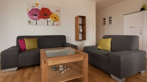 Ein modernes Wohnzimmer mit zwei grauen Sofas, einem Glastisch und einem Holztisch mit Dekoration.