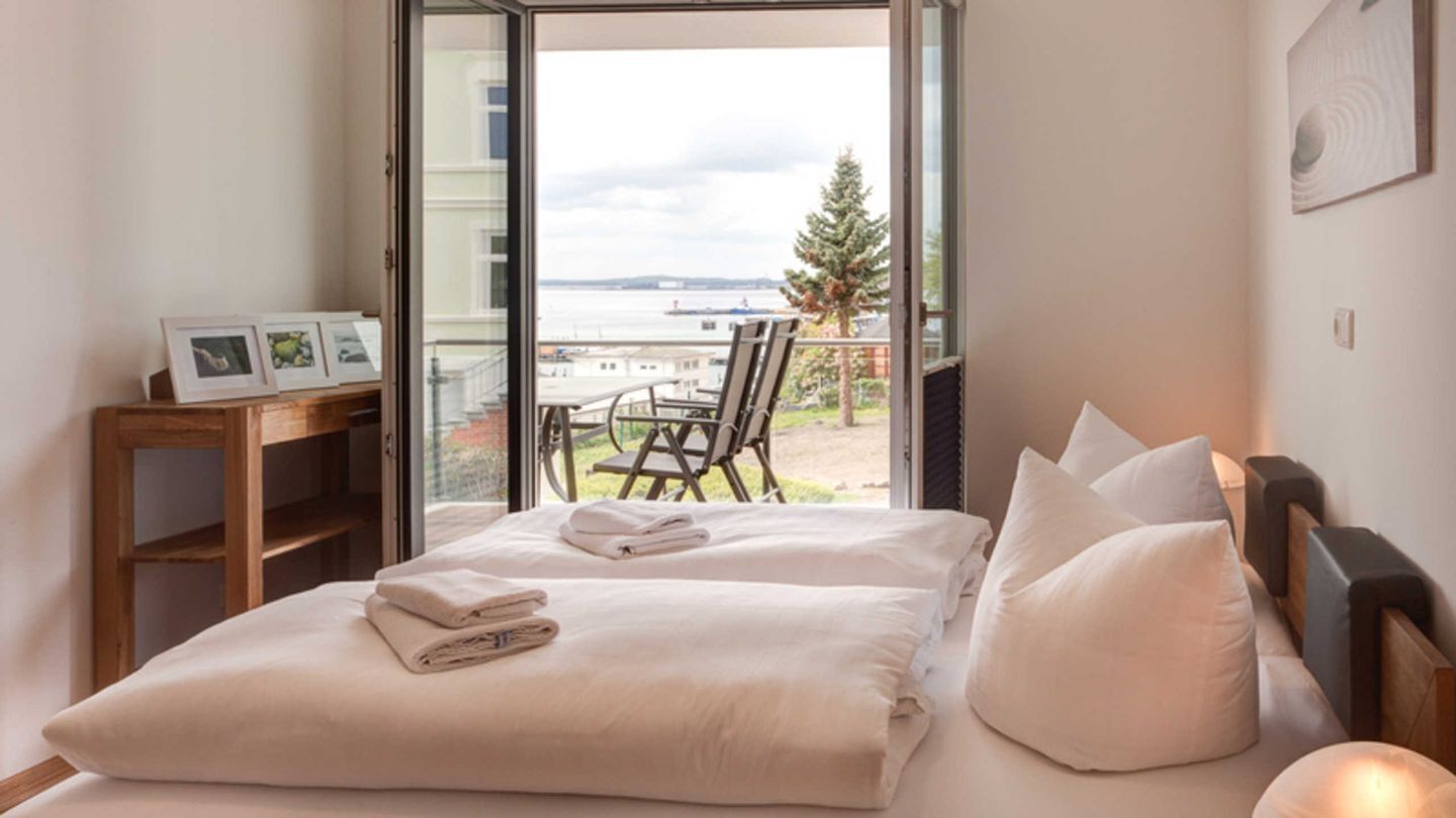 Quarto com cama, almofadas, mesa de cabeceira e vista para o exterior.
