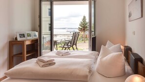 Une chambre à coucher avec un lit, des oreillers, une table de chevet et une vue sur l’extérieur.