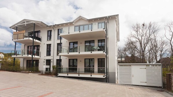Un immeuble résidentiel moderne à plusieurs étages, doté de balcons, de grandes fenêtres et d’une entrée sécurisée par un portail.