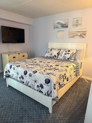 A bedroom with a bed, a TV, a dresser, and wall art.