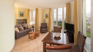 Ein Wohnzimmer mit Sofa, Sessel, Fernseher und Esstisch.