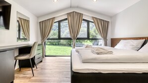 Une chambre avec un grand lit, un bureau et une vue sur la verdure.