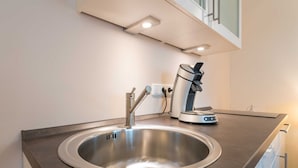 Une cuisine moderne dotée d’un évier en acier inoxydable, d’une machine à café et d’un plan de travail élégant.