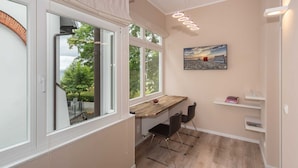 Une cuisine moderne avec un plan de travail en bois, deux chaises noires, un luminaire suspendu et une vue sur l’extérieur grâce à de grandes fenêtres.