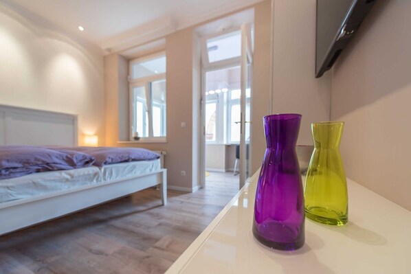 Une chambre à coucher avec un lit, un téléviseur fixé au mur et deux vases posés sur une table de chevet.
